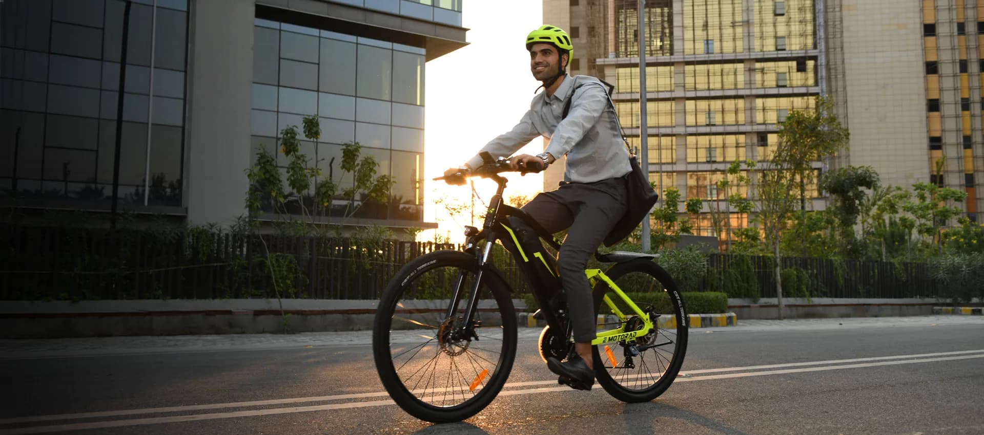 A commuter in office wear riding an EMotorad e-cycle past a glass office building at sunset